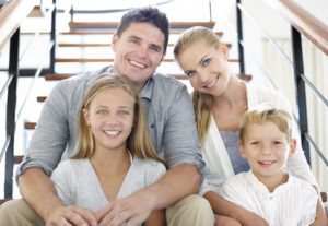 Family of 4 sitting on stairs smiling with healthy bright smiles.