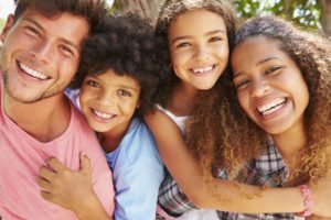 Mixed race family of 4 hanging out with healthy smiles from good oral health care.